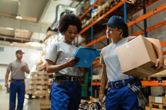 Low angle view of two female workers reading delivery schedule list while working in distribution warehouse.