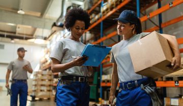 Low angle view of two female workers reading delivery schedule list while working in distribution warehouse.