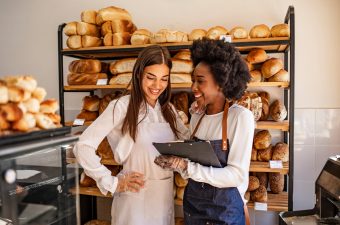 Two beautiful young bakers at the bakery. Shot of a young woman showing her colleague something on her clipboard while they stand in their bakery shop. Smiling young bakers at the bakery shop