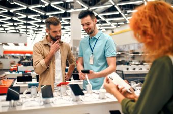 Sales consultant advises man who chooses new smartphone in store of household appliances, electronics and gadgets. Professional consultation in store. Sale Day.