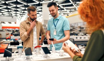 Sales consultant advises man who chooses new smartphone in store of household appliances, electronics and gadgets. Professional consultation in store. Sale Day.