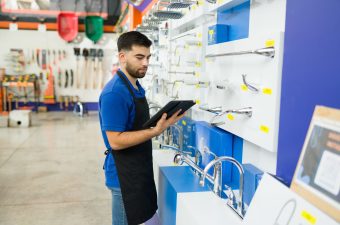 Attractive caucasian man reading from a clipboard and looking for a product or tool for a customer while working at the hardware store