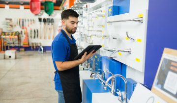 Attractive caucasian man reading from a clipboard and looking for a product or tool for a customer while working at the hardware store